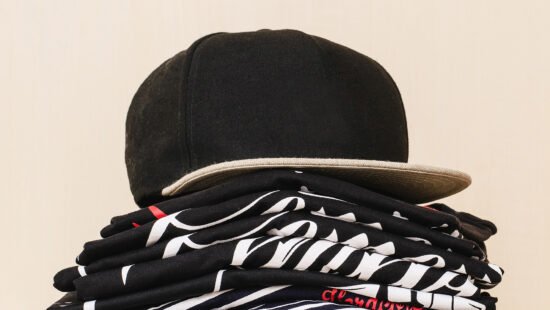 Pile-of-brand-new-t-shirts,-dark-tones,-with-print-and-a-black-straight-flap-cap-over-the-pile